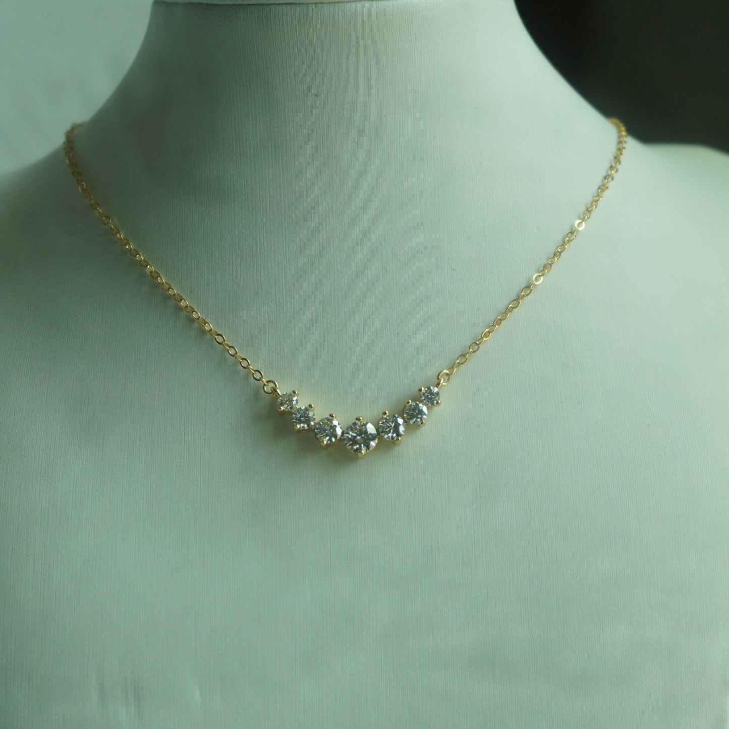 Gold necklace on a mannequin bust against a plain background