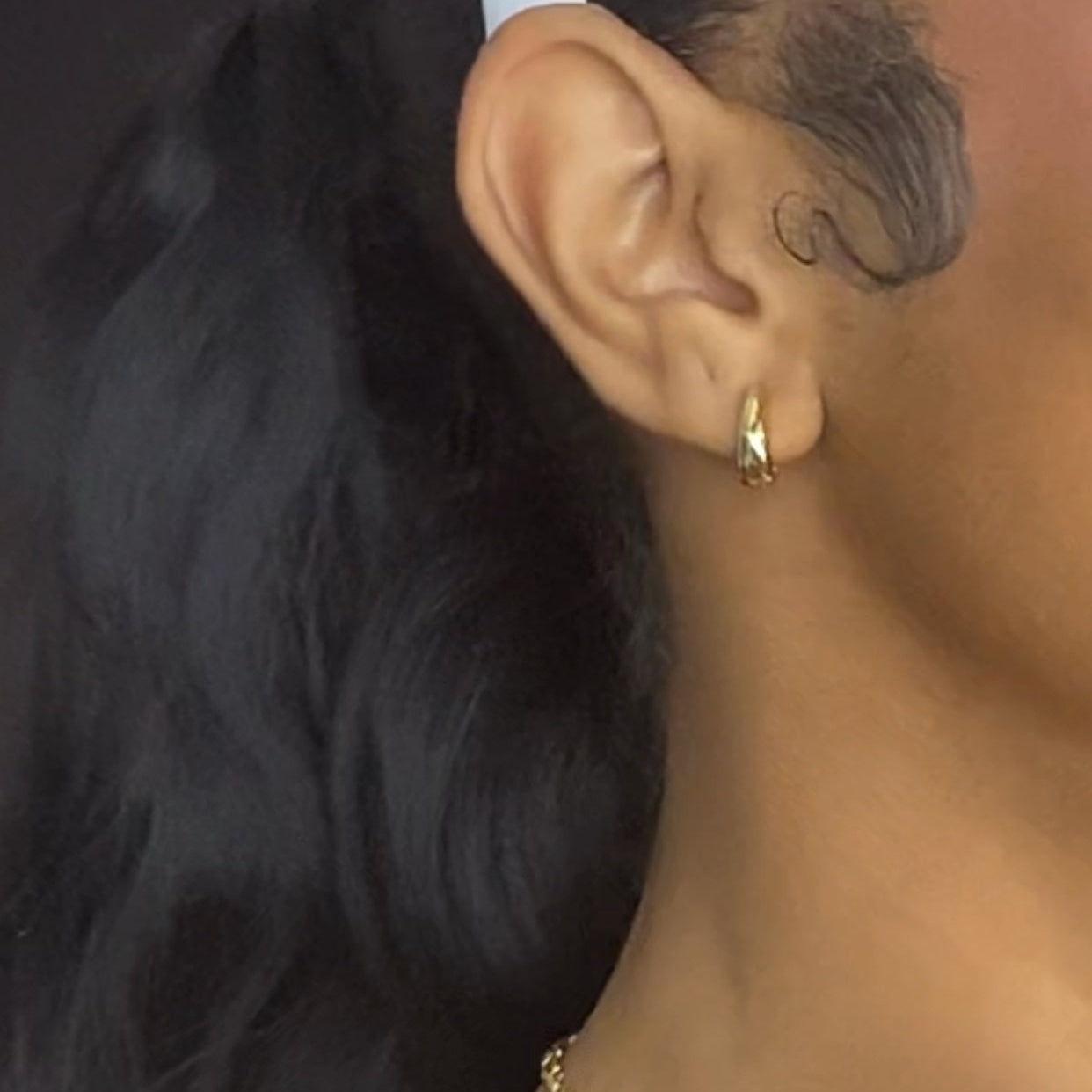 Close-up of an ear with a gold earring and hair, focusing on the jewelry.