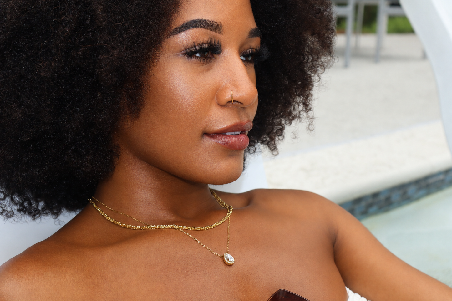 Woman with an afro wearing gold jewelry by a poolside