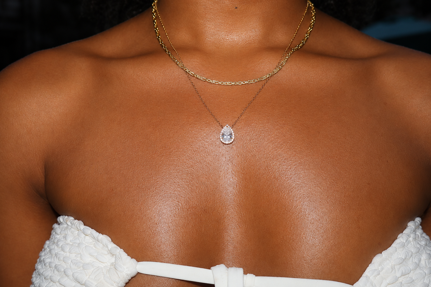 Close-up of a person wearing a gold necklace with a pendant on a dark background